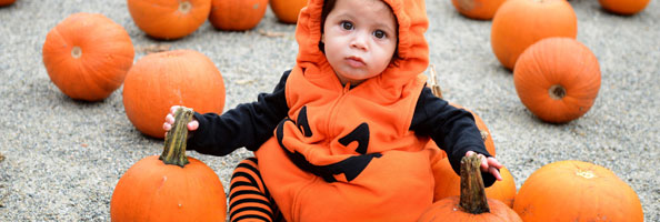 Baby in a jack-o-lantern costume sitting among pumpkins