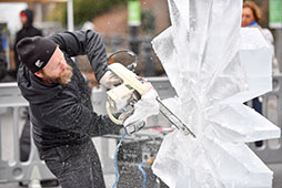 a man uses a saw to sculpt ice into a winter-themed design