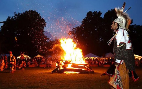 a man dressed in traditional garb stand around a fire as guests look on