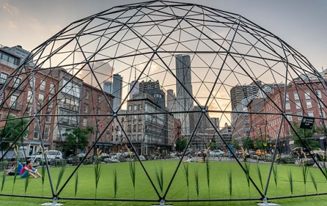guests hang out on a synthetic turf under a dome in the middle of a plaza surrounded by skyscrapers