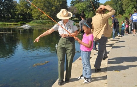 a park ranger teaches a girl how to fish at a lake